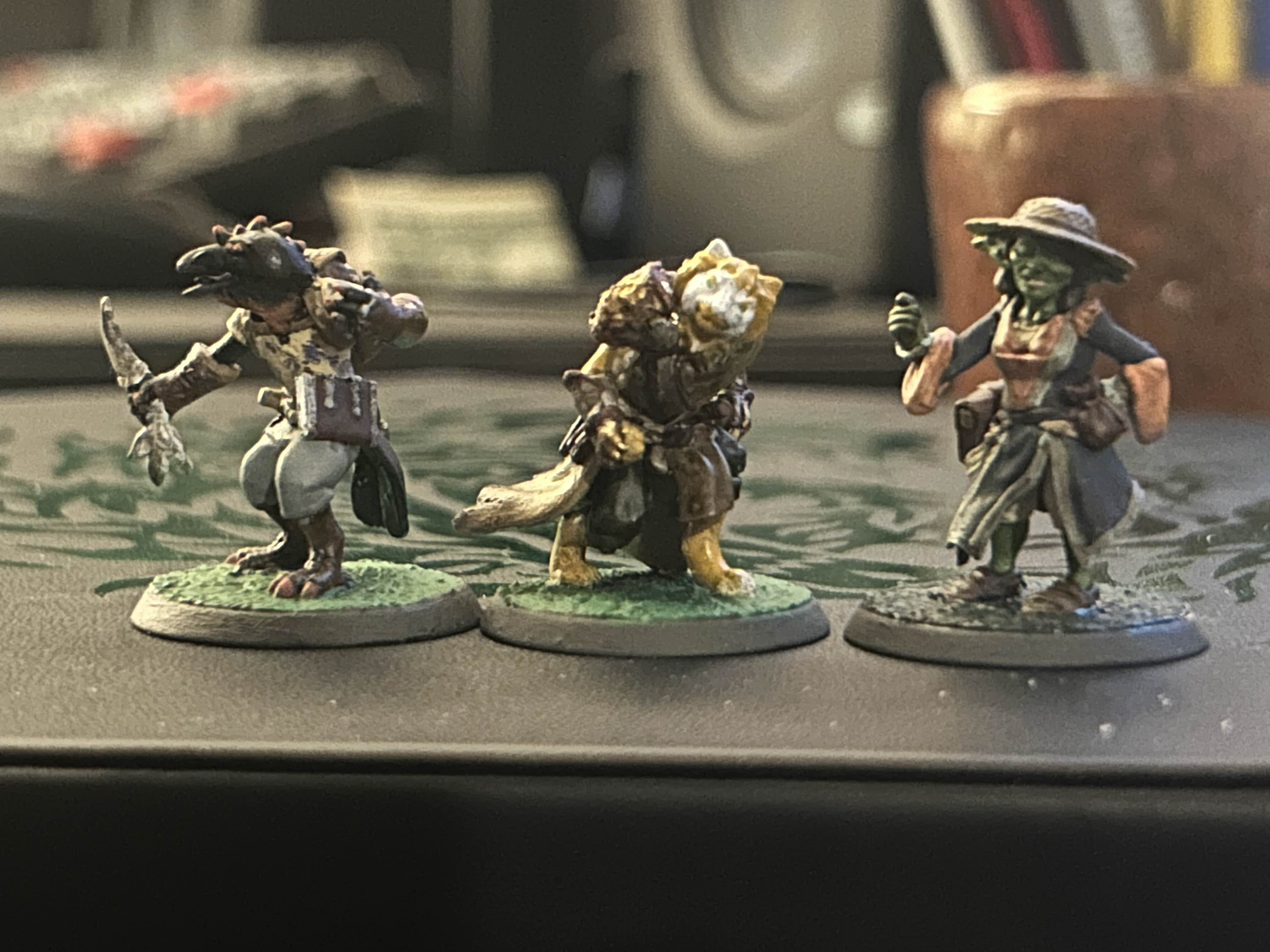 Image of three minifigures. From left to right is a kenku with a dagger, an orange and white tabaxi sneaking, and a goblin woman looking indignant. They are painted very expertly and look really really cool.